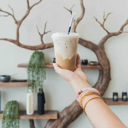 Latte drink held in front of Moxie Coffee Bar’s branch shelving.