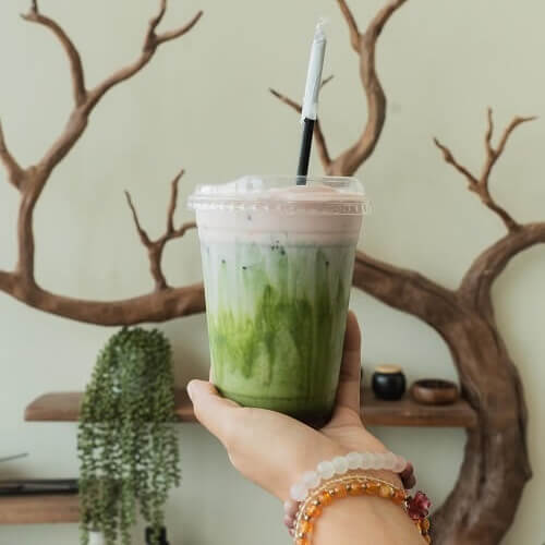 Iced green matcha drink held in front of Moxie Coffee Bar’s branch shelving.